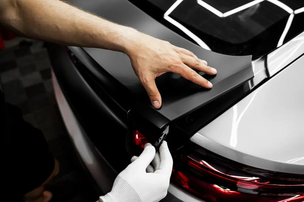 Hand peeling black vinyl wrap film off a white car panel