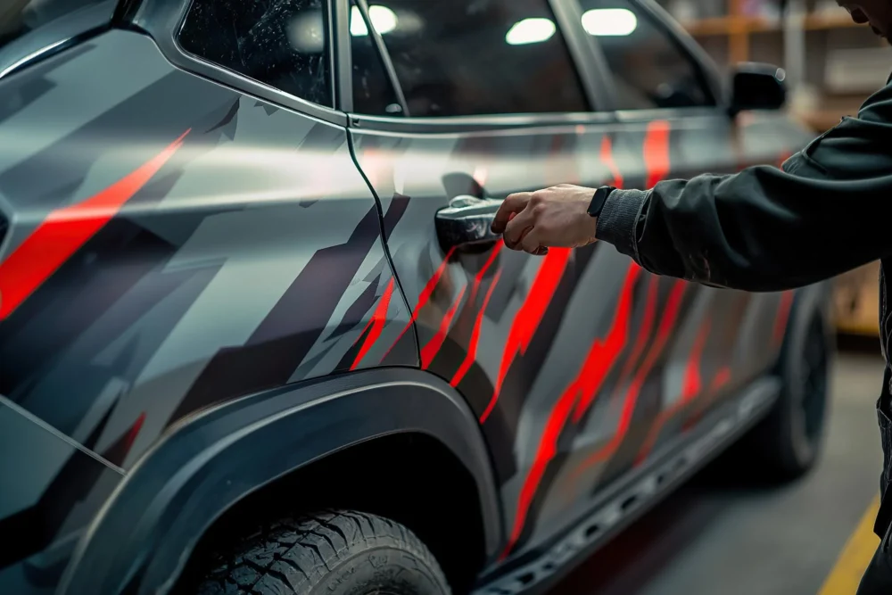 Installer fitting red and grey graphic wrap to a vehicle panel