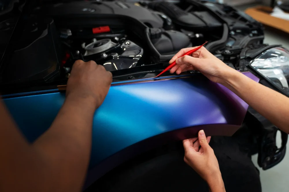 Installer smoothing blue vinyl wrap film onto a car panel
