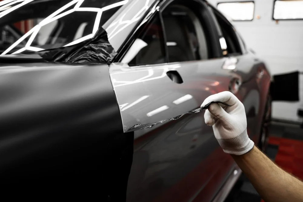 Gloved hand smoothing silver satin wrap film on a car door